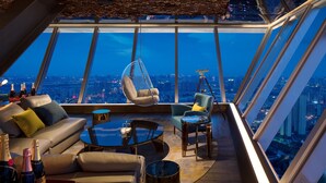 Un interior d'un edifici alt amb vista a la ciutat, una cadira penjant, un sofà i una taula de cafè.