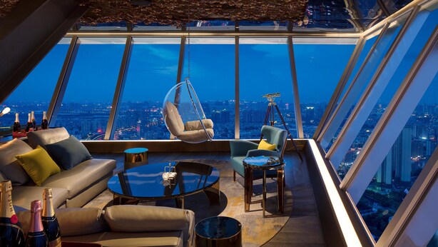 Un intérieur moderne situé dans un immeuble de grande hauteur, avec vue sur la ville, comprenant un fauteuil suspendu, un canapé et une table basse.