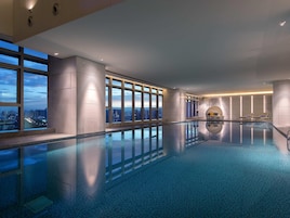 Una piscina interior moderna con vistas a la ciudad, amplios ventanales y un diseño minimalista.