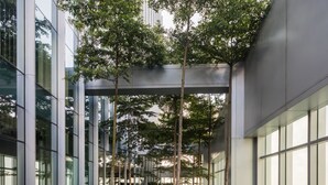Un bâtiment moderne doté d’un élément décoratif aquatique réfléchissant, de murs en verre et d’un espace extérieur aménagé pour s’asseoir.