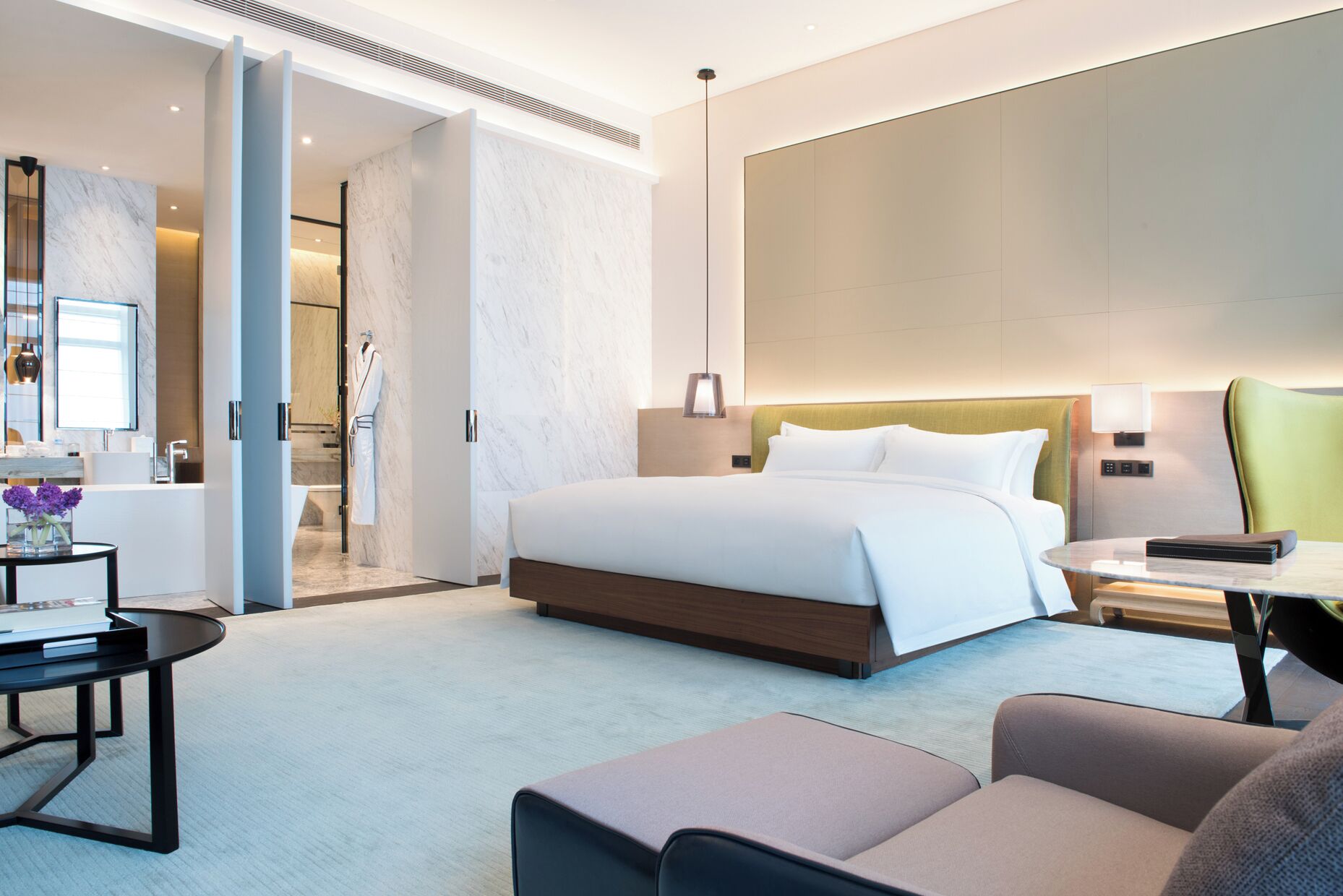 A modern hotel room with a large bed, a desk, a chair, and a bathroom visible through an open door.