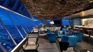 Un bar modern ubicat en un gratacels, amb vistes panoràmiques a la ciutat, mobles actuals i un disseny de sostre únic.