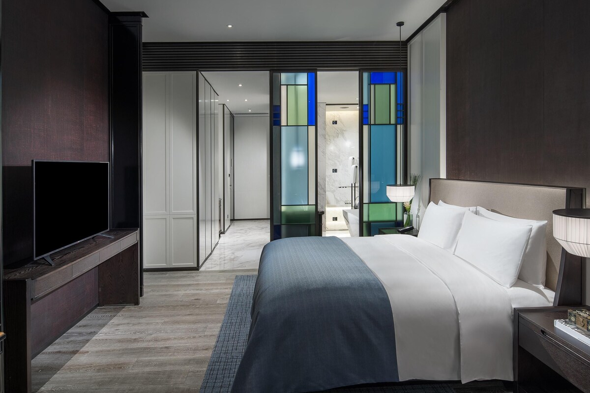 Ein modernes Hotelzimmer mit einem großen Bett, einem Flachbildfernseher, einem Nachttisch und einem begehbaren Kleiderschrank.