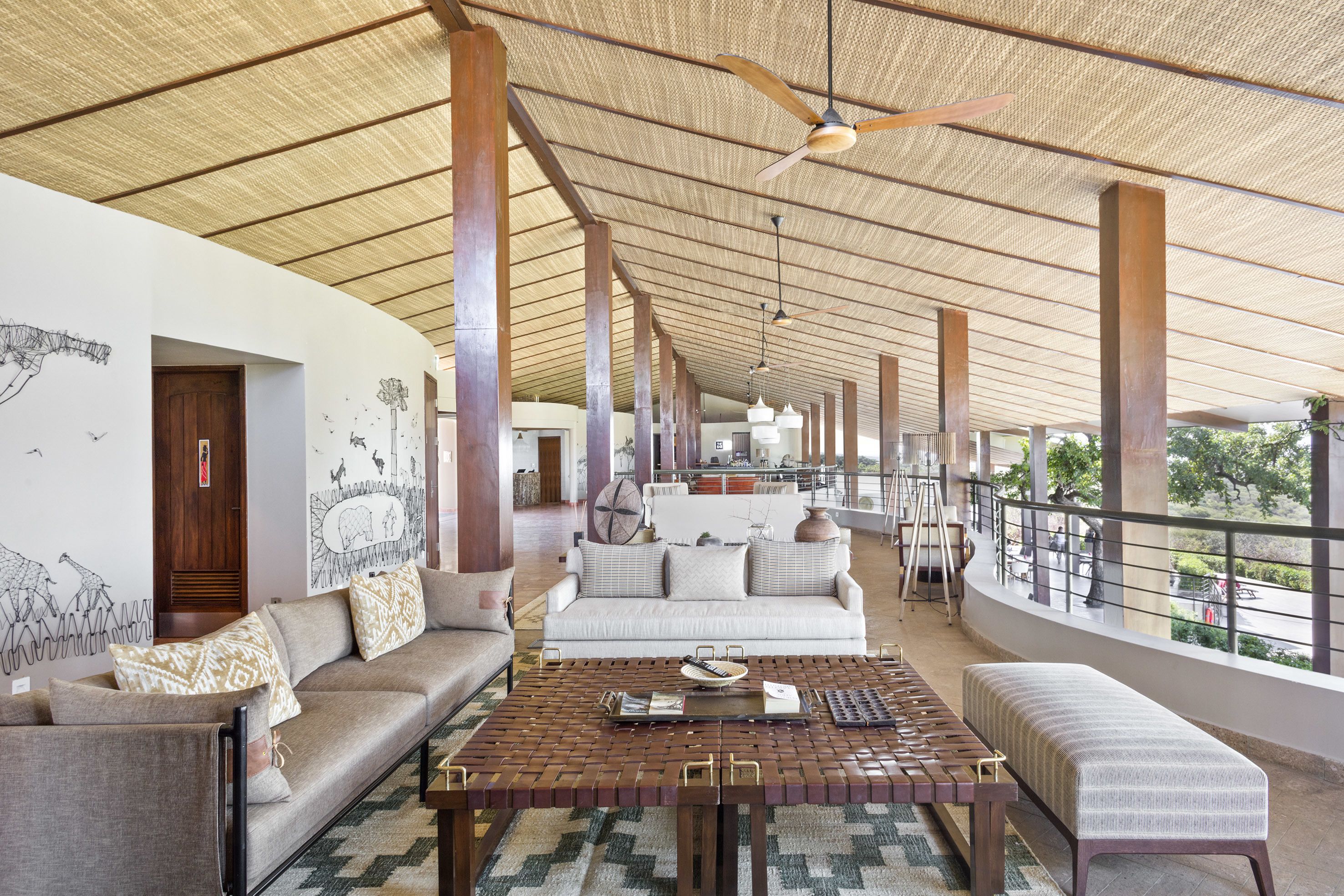 A spacious indoor area with a high ceiling, a wooden table, a sofa, and a balcony with a railing.