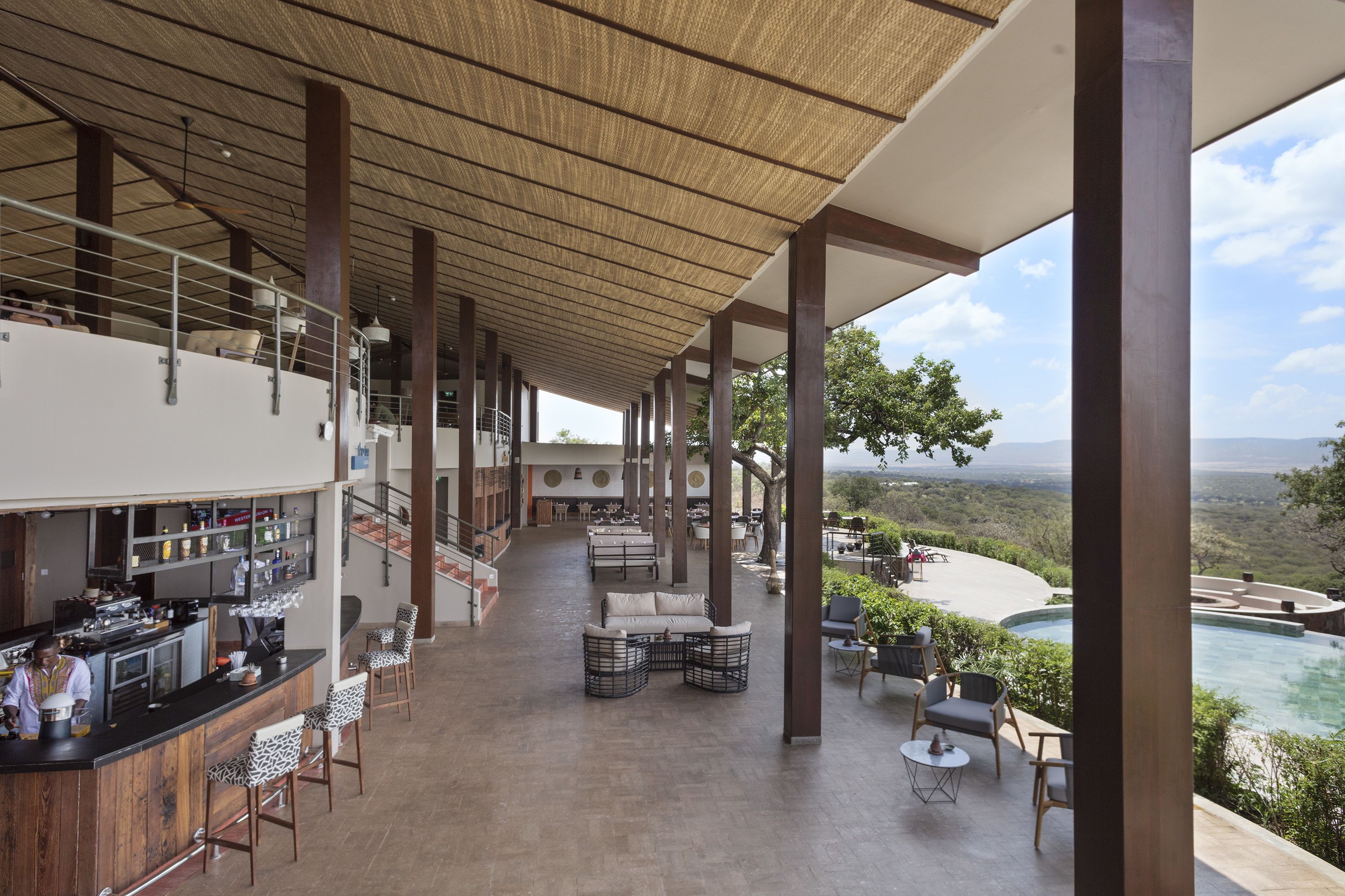 Un'ampia area interna con un bar, posti a sedere e vista su una piscina e il paesaggio.