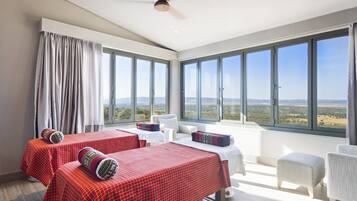 Two beds with checkered bedding and decorative pillows, a white armchair, and ottoman, set against a backdrop of the surrounding landscape.