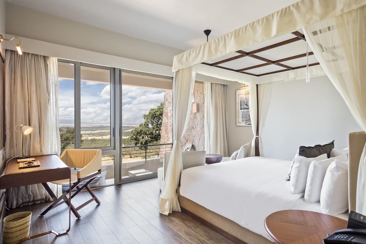 Une chambre avec un grand lit, un bureau, une chaise et une vue sur l’extérieur.
