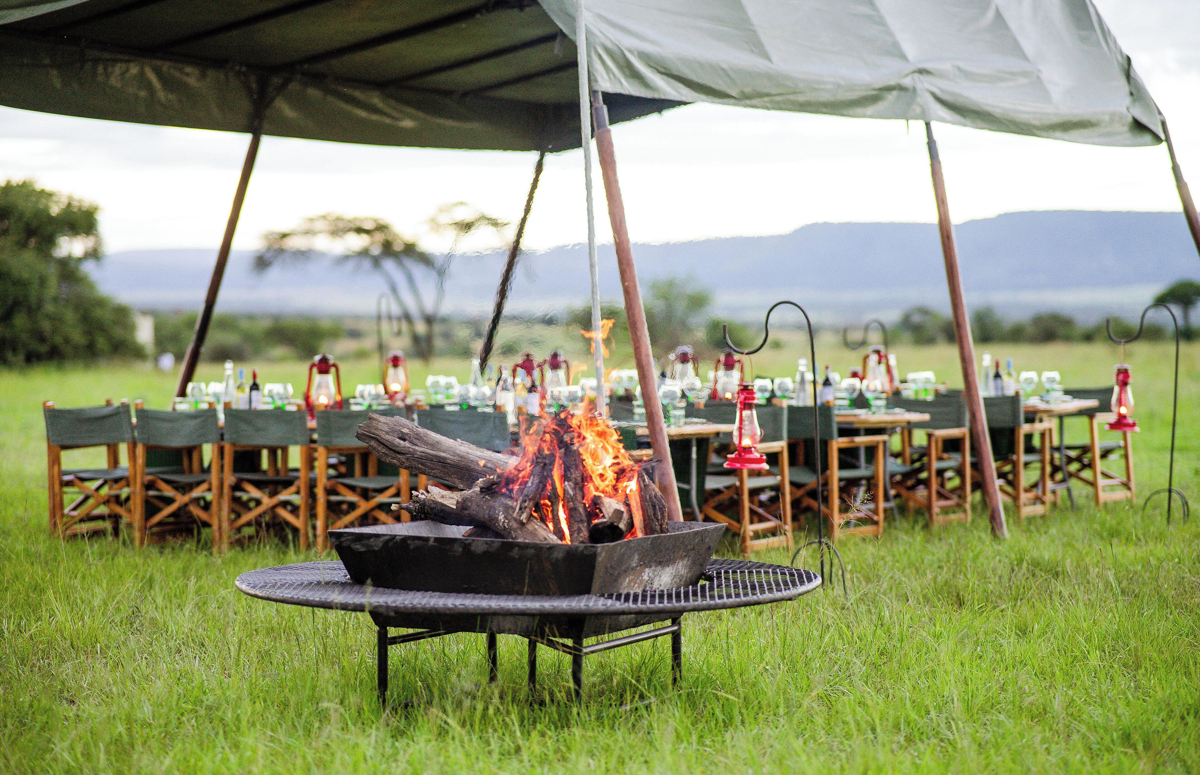 An outdoor dining area with a fire pit, tables, chairs, and a tent.
