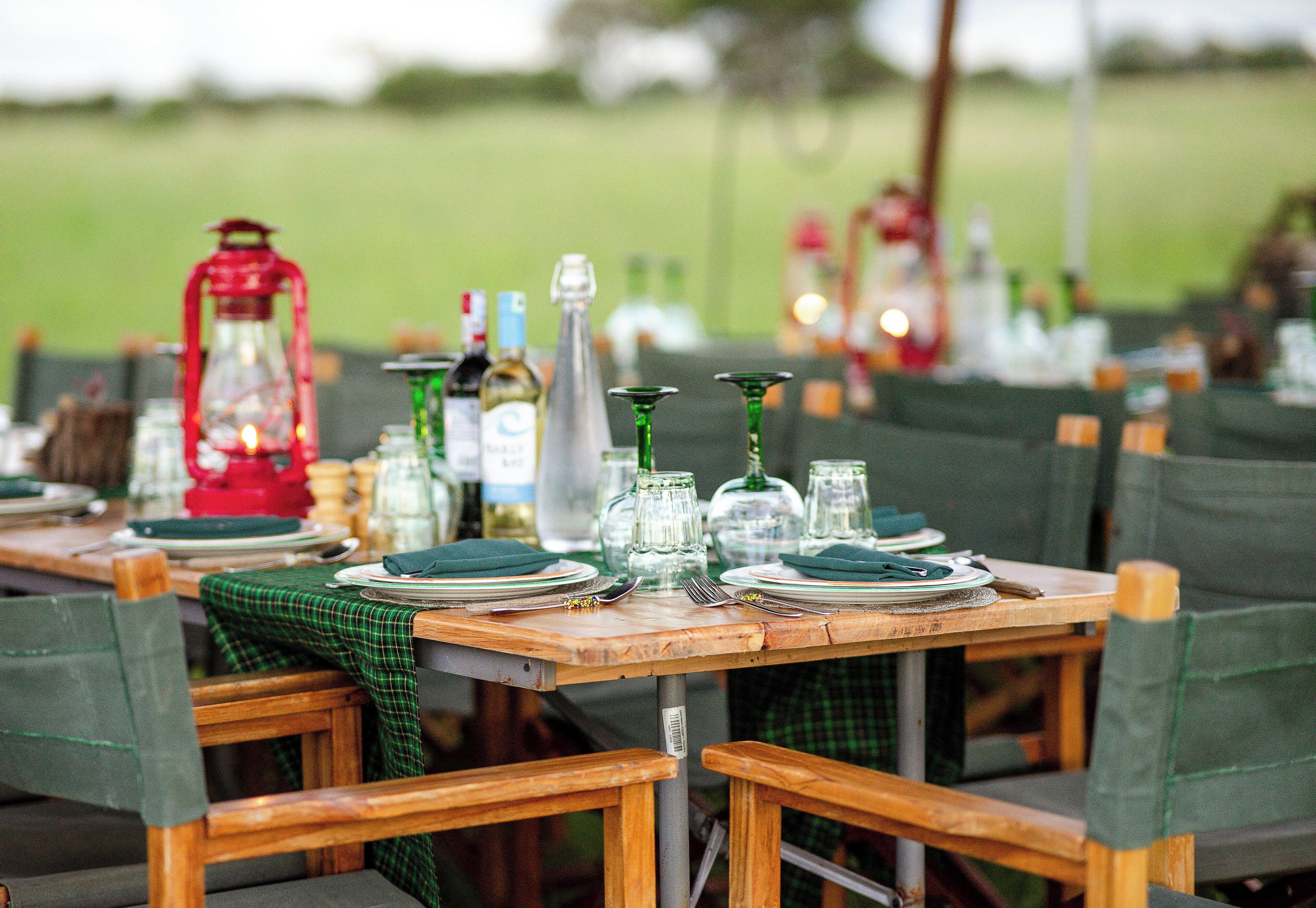 A dining table set with plates, glasses, and cutlery, surrounded by chairs with green upholstery.