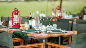 A dining table set with plates, glasses, and cutlery, surrounded by chairs with green upholstery.
