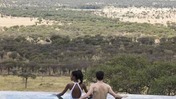 Ein Paar entspannt am Infinity-Pool mit Blick auf eine Savannenlandschaft.