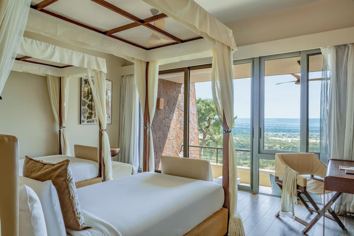 Une chambre d’hôtel avec un grand lit, deux tables de chevet, une chaise et un balcon avec vue.
