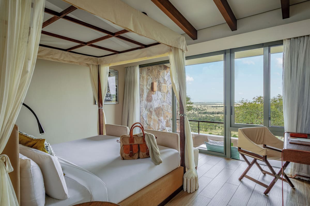 Une chambre avec un grand lit, une vue sur l’extérieur et un balcon avec une chaise.