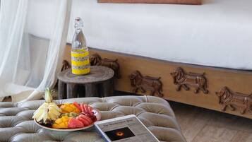 A neatly made bed with a tray of breakfast items, a bottle, and a tablet on a cushioned bench.