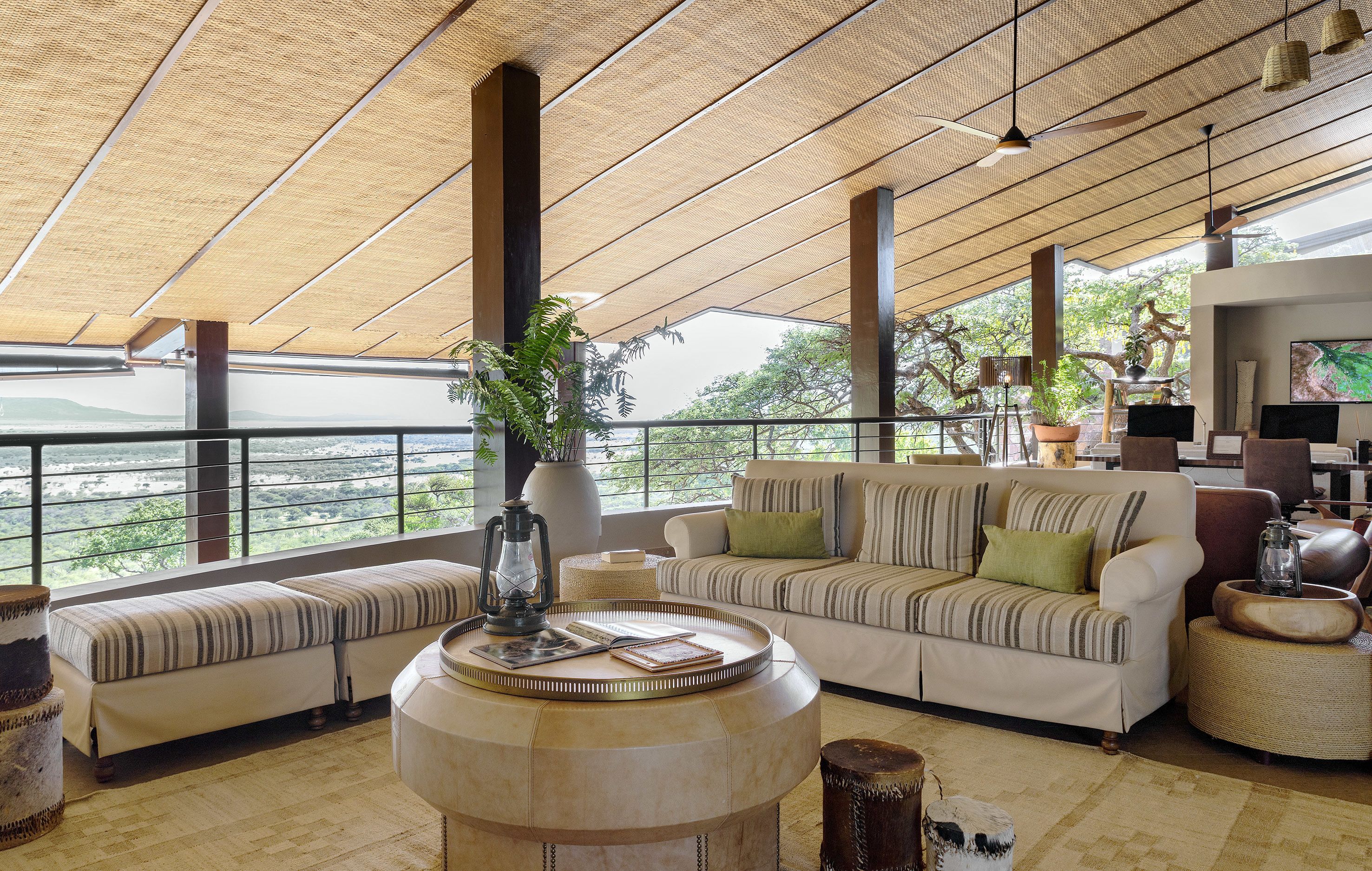 A spacious lounge with a high ceiling, large windows, a sofa set, a coffee table, and a television.