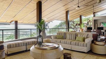 A spacious lounge with a high ceiling, large windows, a sofa set, a coffee table, and a television.