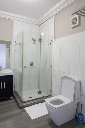 A bathroom with a glass-enclosed shower, a toilet, and a sink.