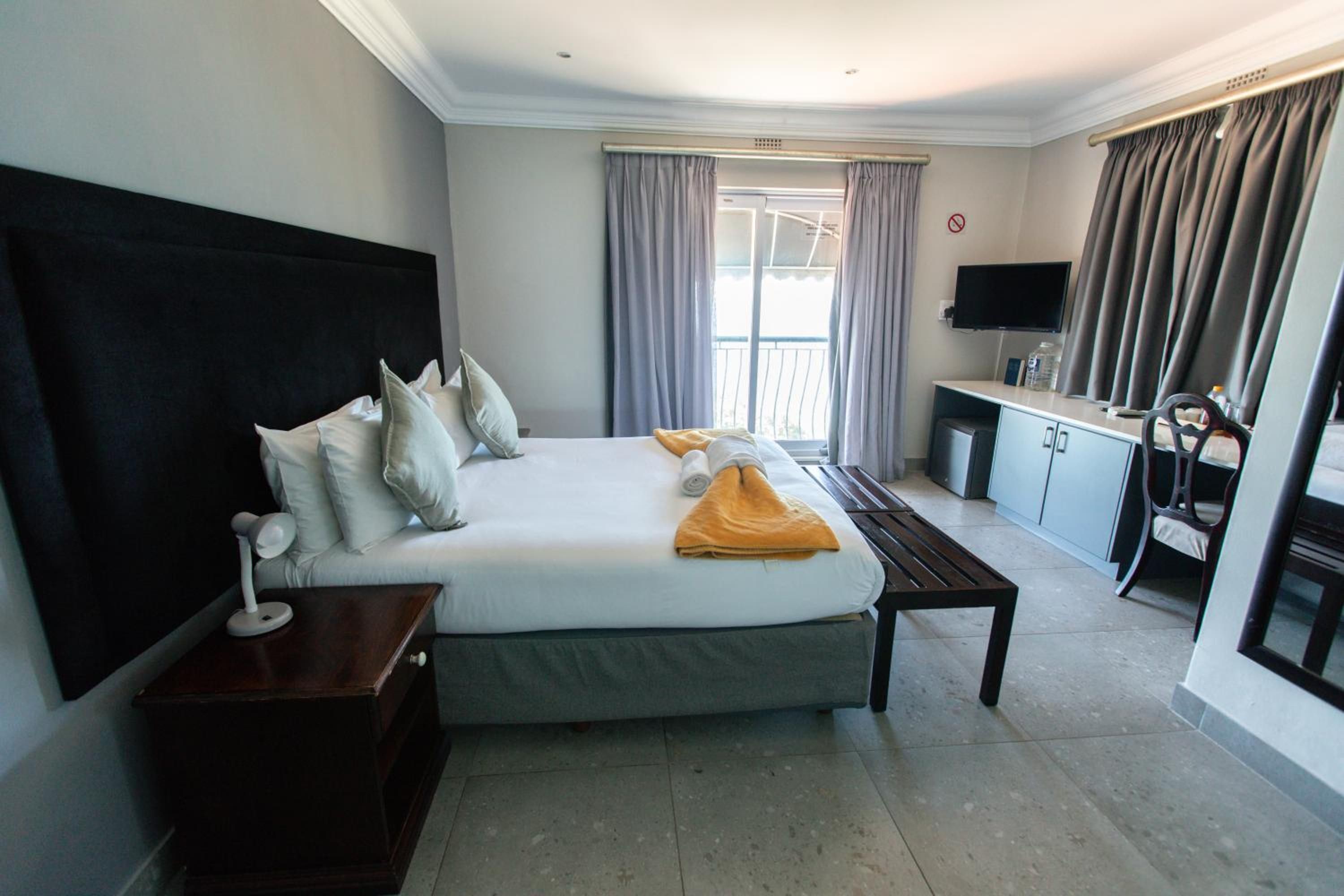 A hotel room with a large bed, a desk, a TV, and a balcony.