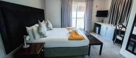 A hotel room with a large bed, a desk, a TV, and a balcony.