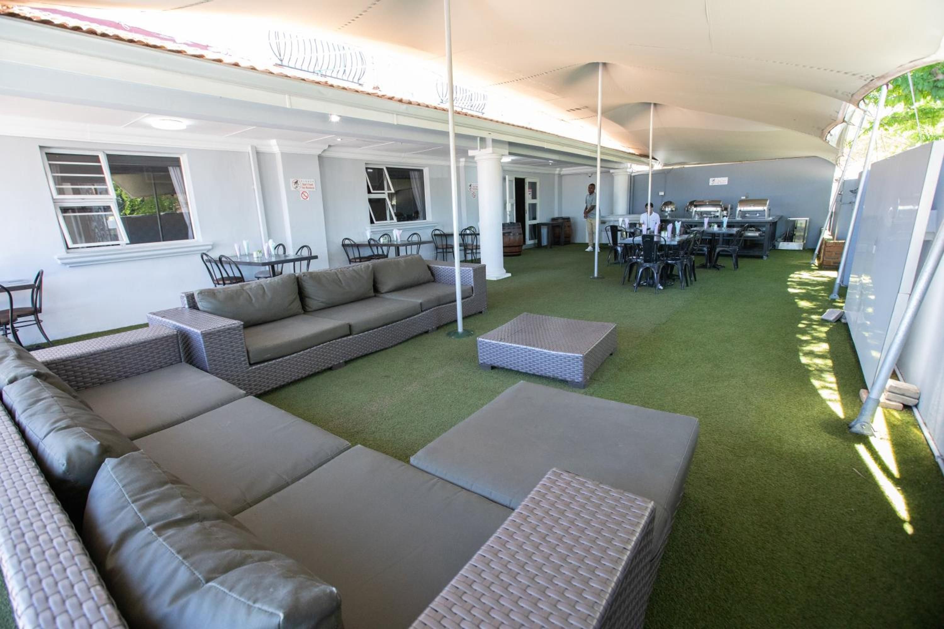 A covered outdoor seating area with a sofa, chairs, and a dining table.
