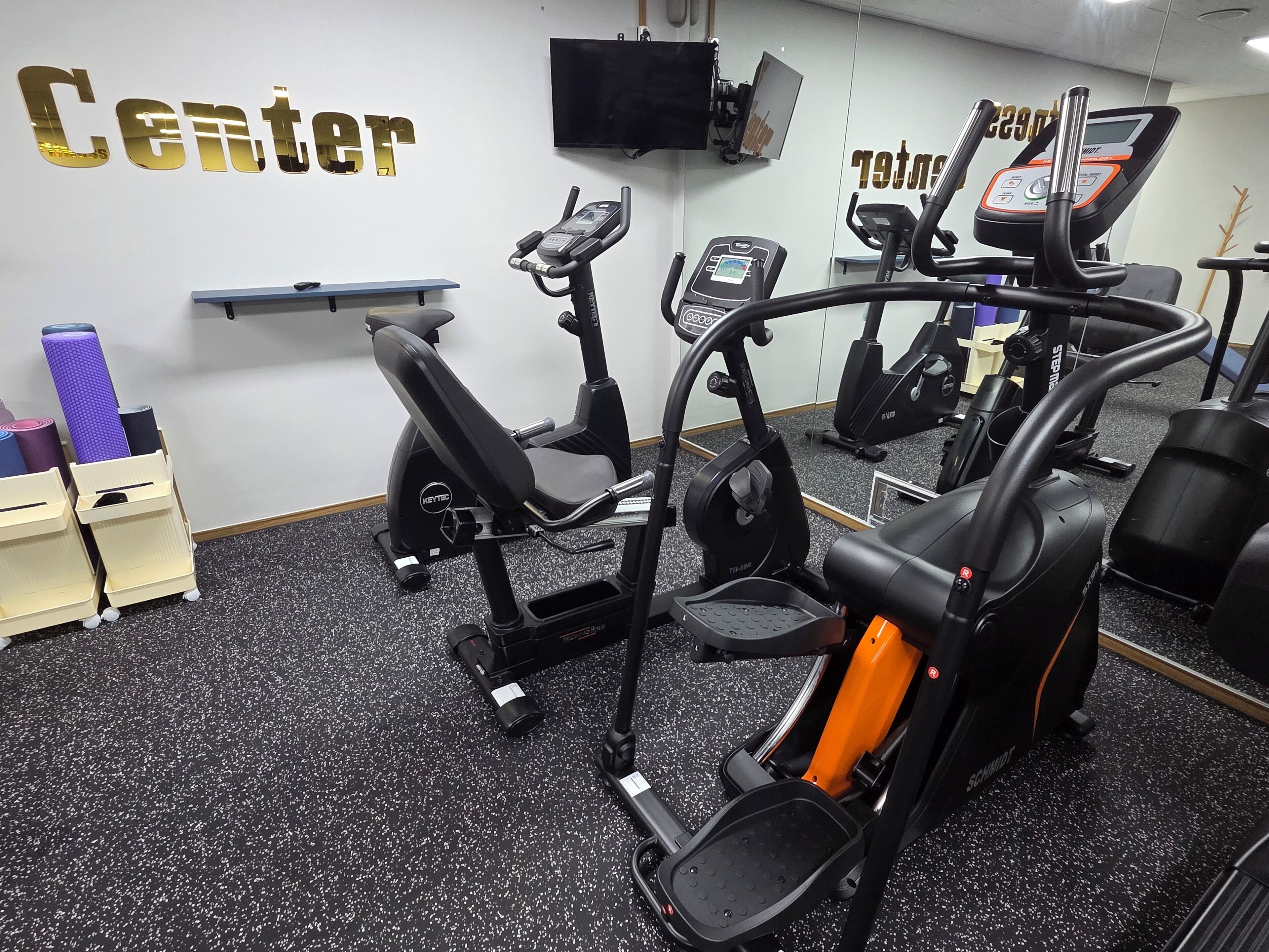 A gym with stationary bikes, treadmills, and a wall-mounted TV.
