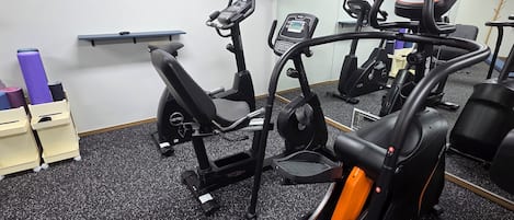 A gym with stationary bikes, treadmills, and a wall-mounted TV.