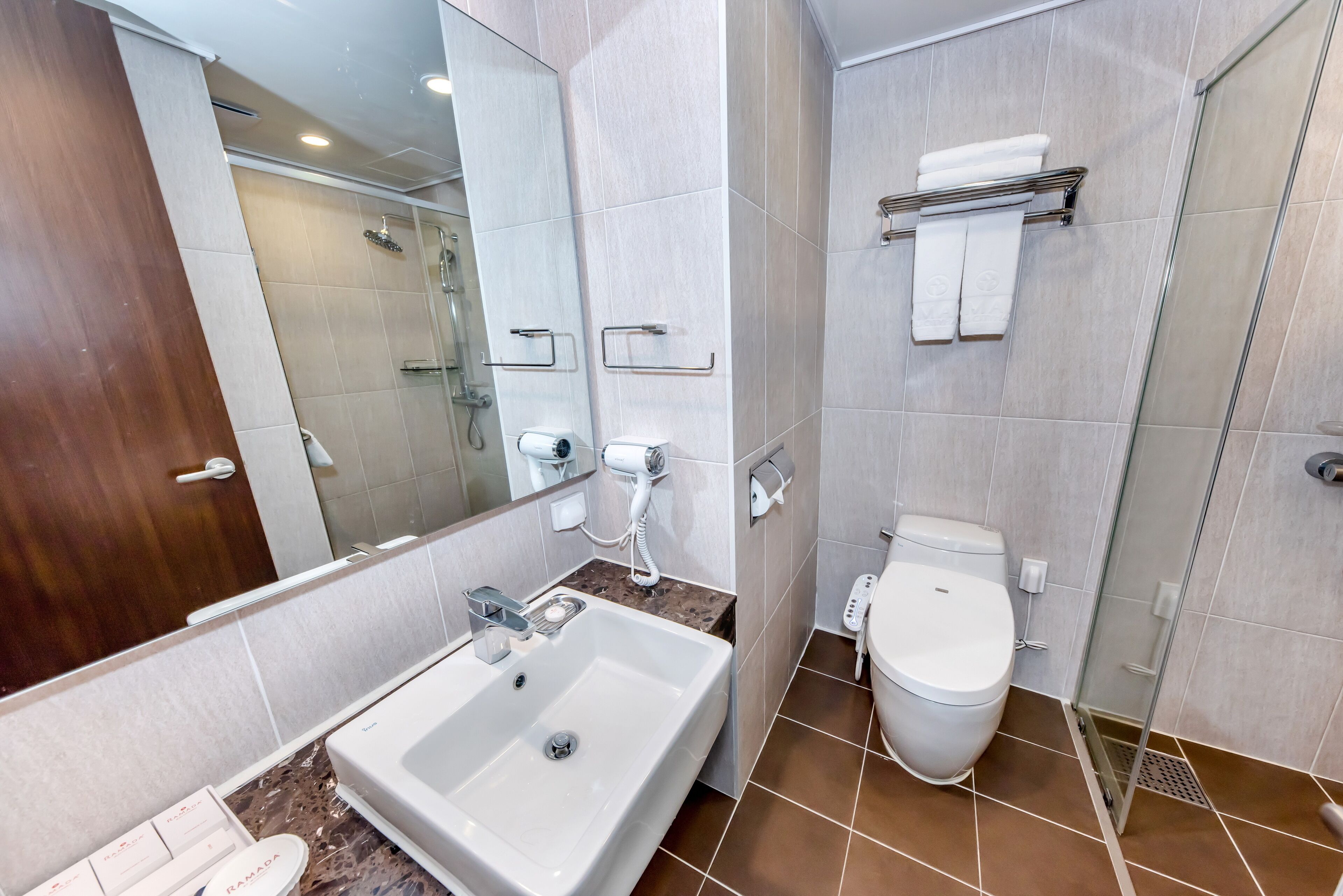 A modern bathroom with a large mirror, a white sink, a toilet, and a shower area.