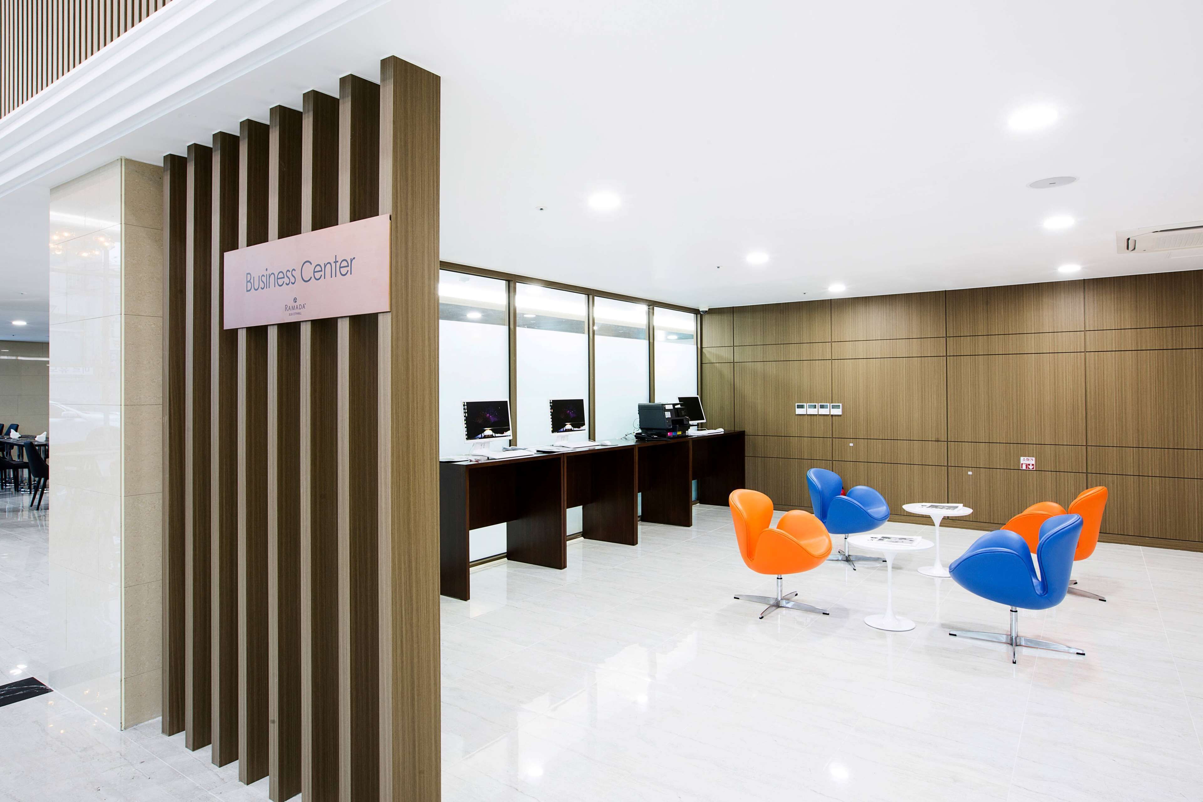 Un centre d’affaires doté d’un comptoir d’accueil, d’ordinateurs et de chaises modernes aux couleurs orange et bleu.