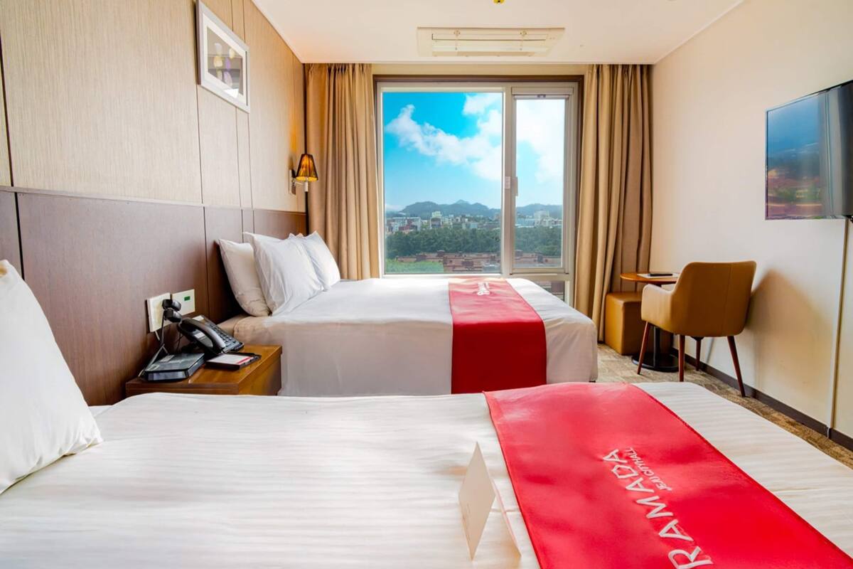 Habitació d'hotel amb dos llits, una taula de treball, una cadira, televisió i una finestra gran amb vista a la ciutat.