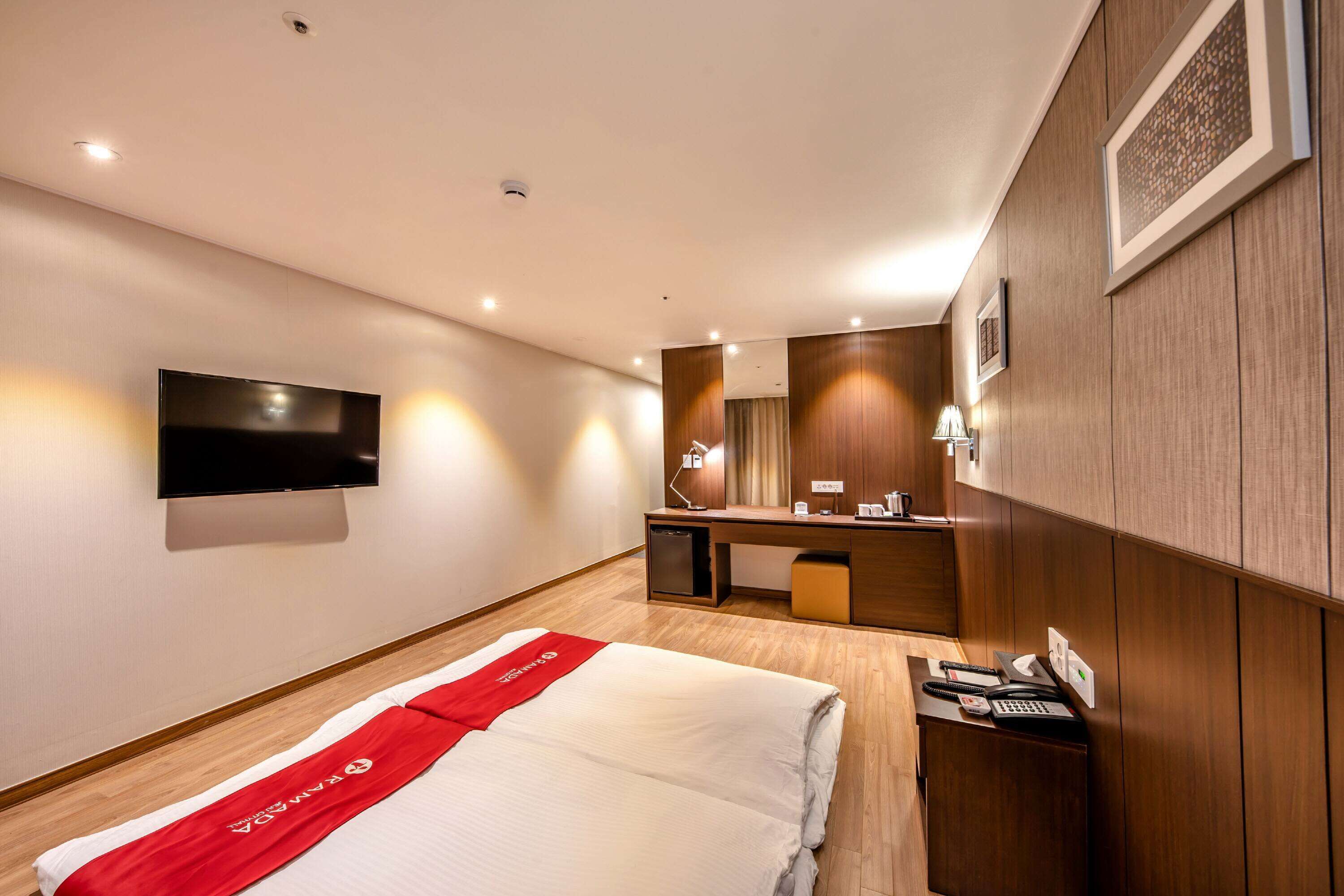 Habitación de hotel con una cama, un escritorio con computadora, un televisor montado en la pared y un mueble auxiliar pequeño.