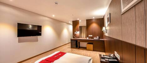 Habitación de hotel con una cama, un escritorio con computadora, un televisor montado en la pared y un mueble auxiliar pequeño.