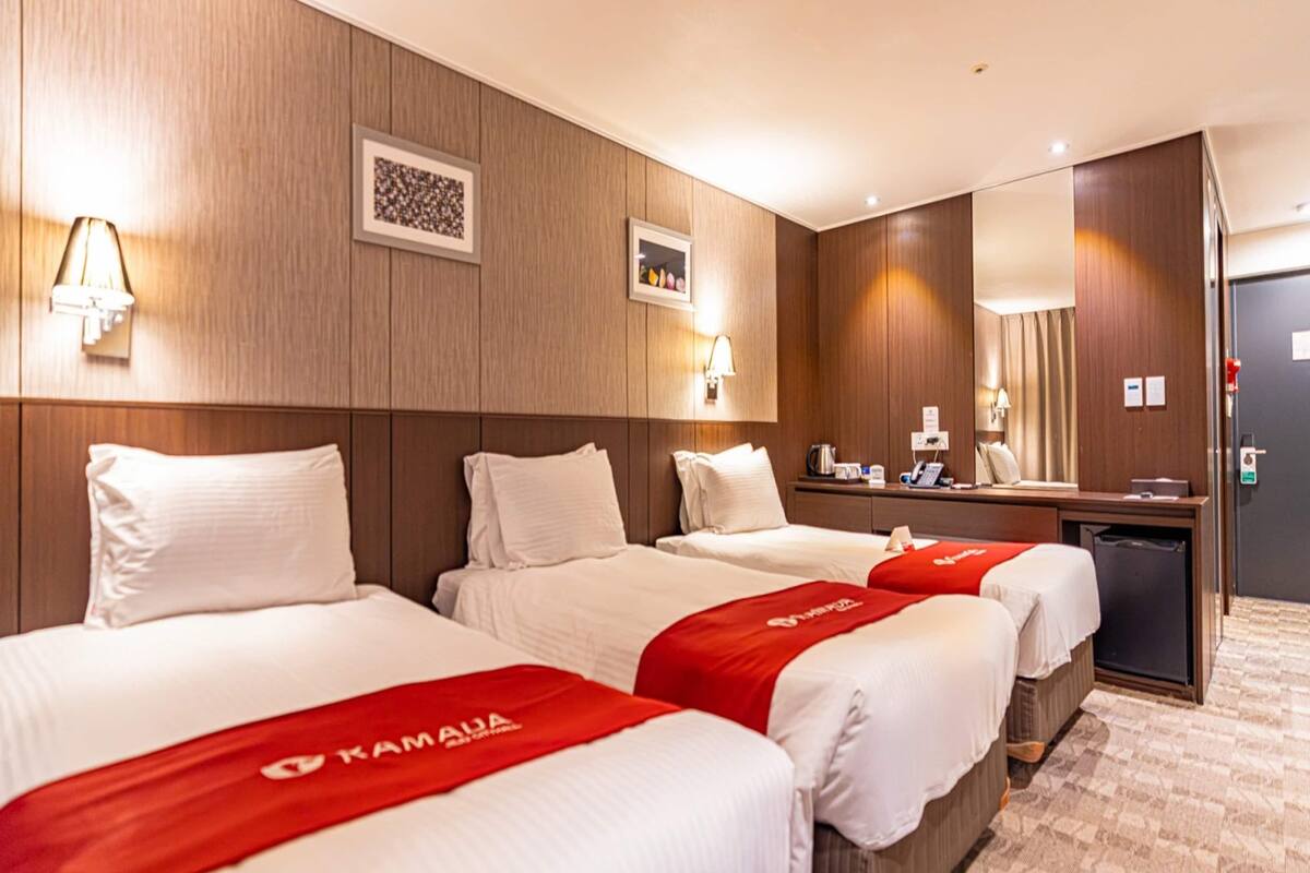 Una habitació d'hotel amb tres llits, un escriptori i un mirall.