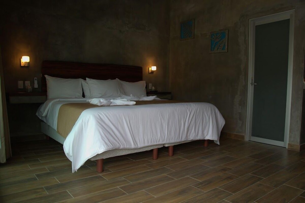 Un lit simple avec une tête de lit en bois, une literie blanche et deux lampes fixées au mur.