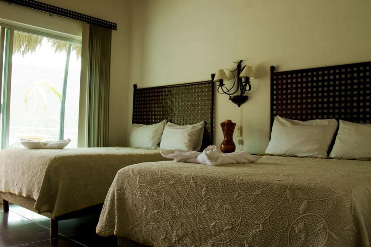 Une chambre d’hôtel avec deux lits, un vase et une lampe fixée au mur.