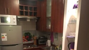 A compact kitchen with wooden cabinets, a built-in oven, and a refrigerator. - Departamento Belen Lira (Santiago)