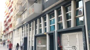A multi-story building with balconies, large windows, and a closed shop with a sign. - Departamento Belen Lira (Santiago)
