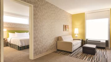 Habitación de hotel con cama, sofá, una mesita, lámpara y ventana con persianas.