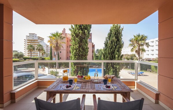 A balcony with a wooden table set for breakfast, overlooking a cityscape with palm trees and buildings.