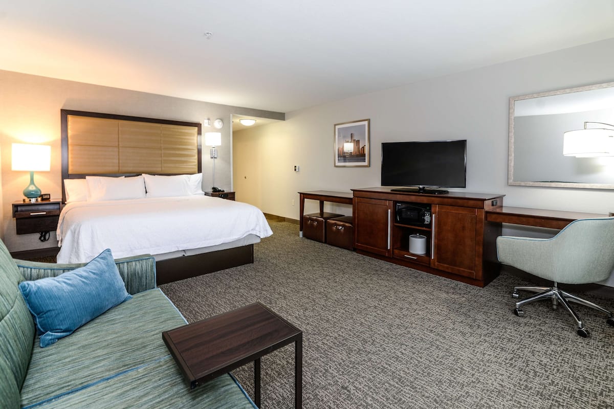 A hotel room with a bed, a desk, a television, a sofa, and a mirror.