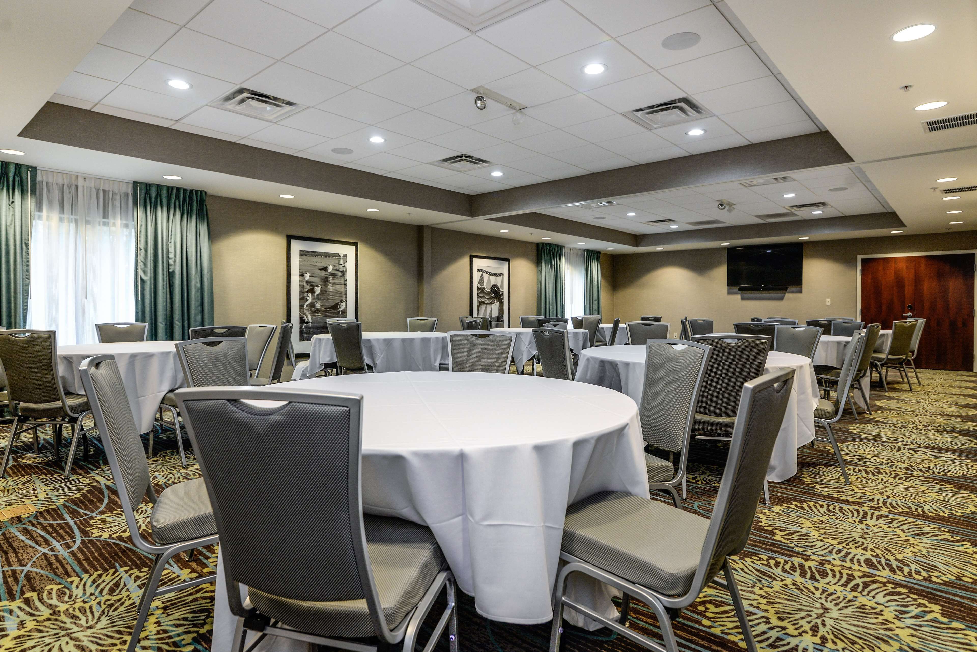 A conference room with round tables and chairs, a patterned carpet, and a television on the wall.
