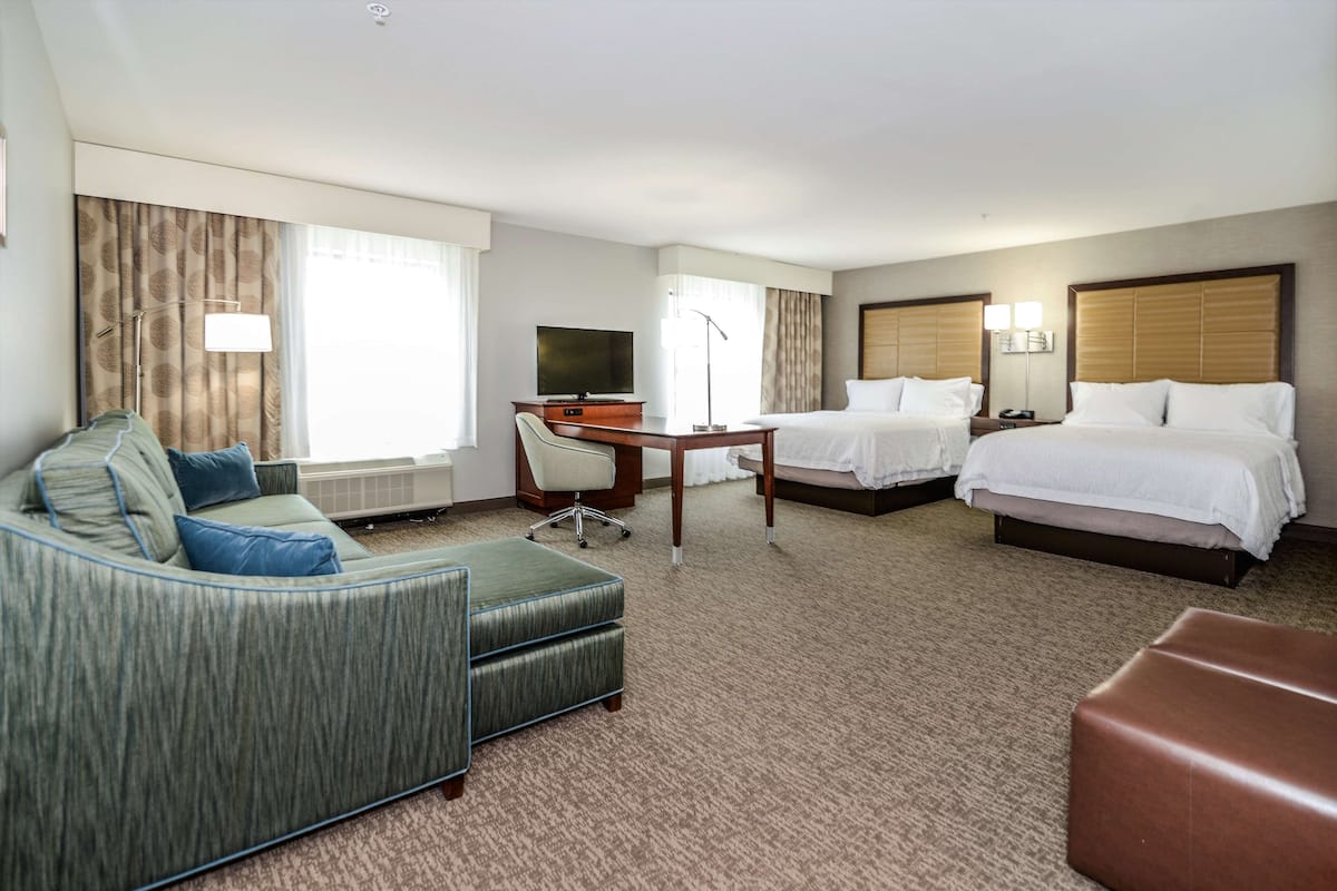 A hotel room with a sofa, a desk, two beds, and a television.