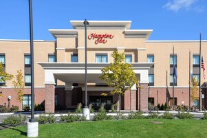 A Hampton Inn hotel with a brick facade, multiple windows, and a clear blue sky.