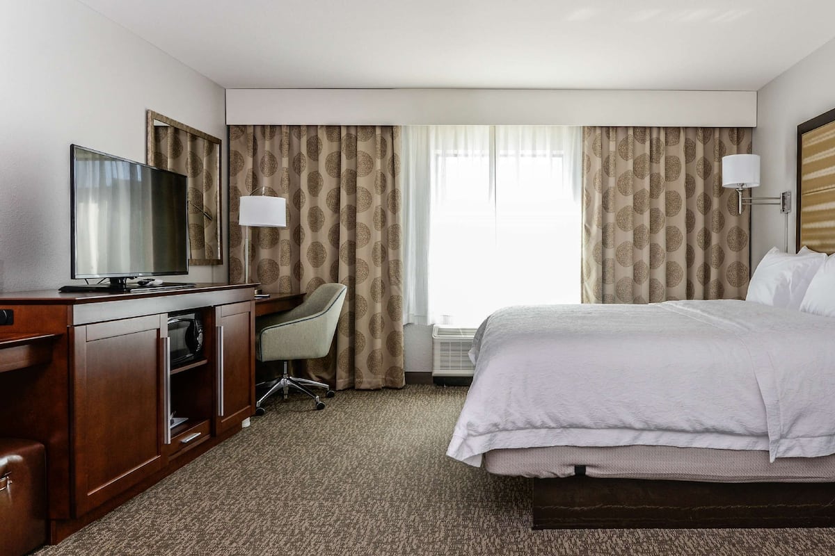 A hotel room with a bed, a desk, a chair, a TV, and a lamp.