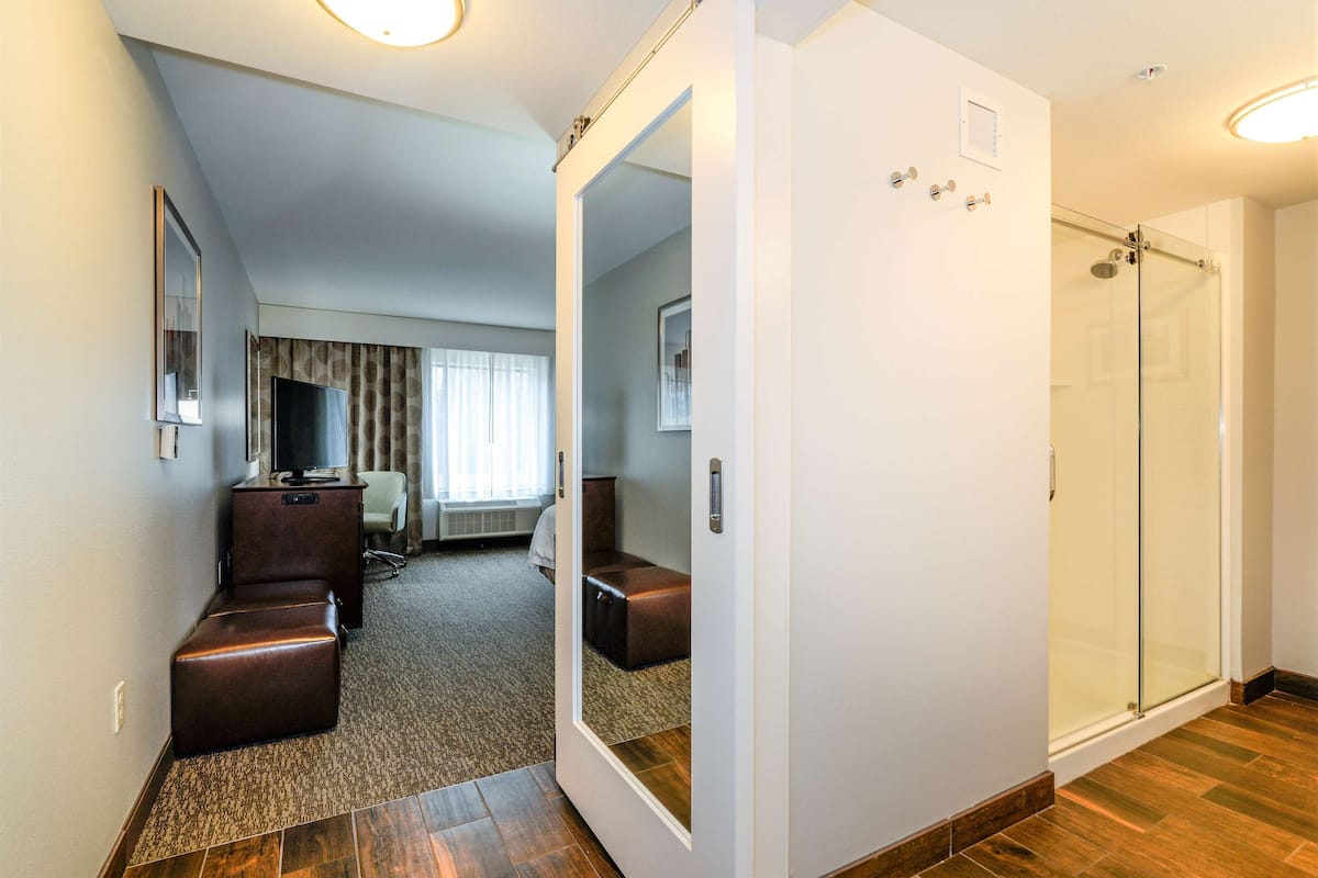 A hotel room with a seating area, a television, a glass shower, and a large mirror.