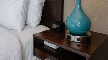 Un lit bien fait, avec du linge de lit blanc, une lampe turquoise posée sur une table de chevet en bois et un petit tiroir.