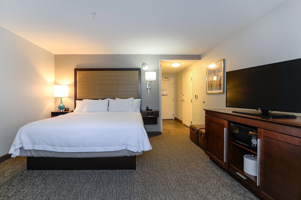 A hotel room with a large bed, bedside lamps, a television, a microwave, and a cabinet.