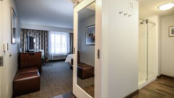 A hotel room with a large mirror, a bed, a seating area, and a shower.