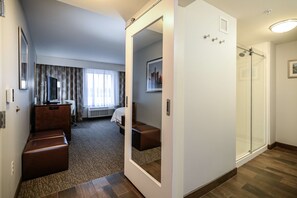 A hotel room with a large mirror, a bed, a seating area, and a shower.