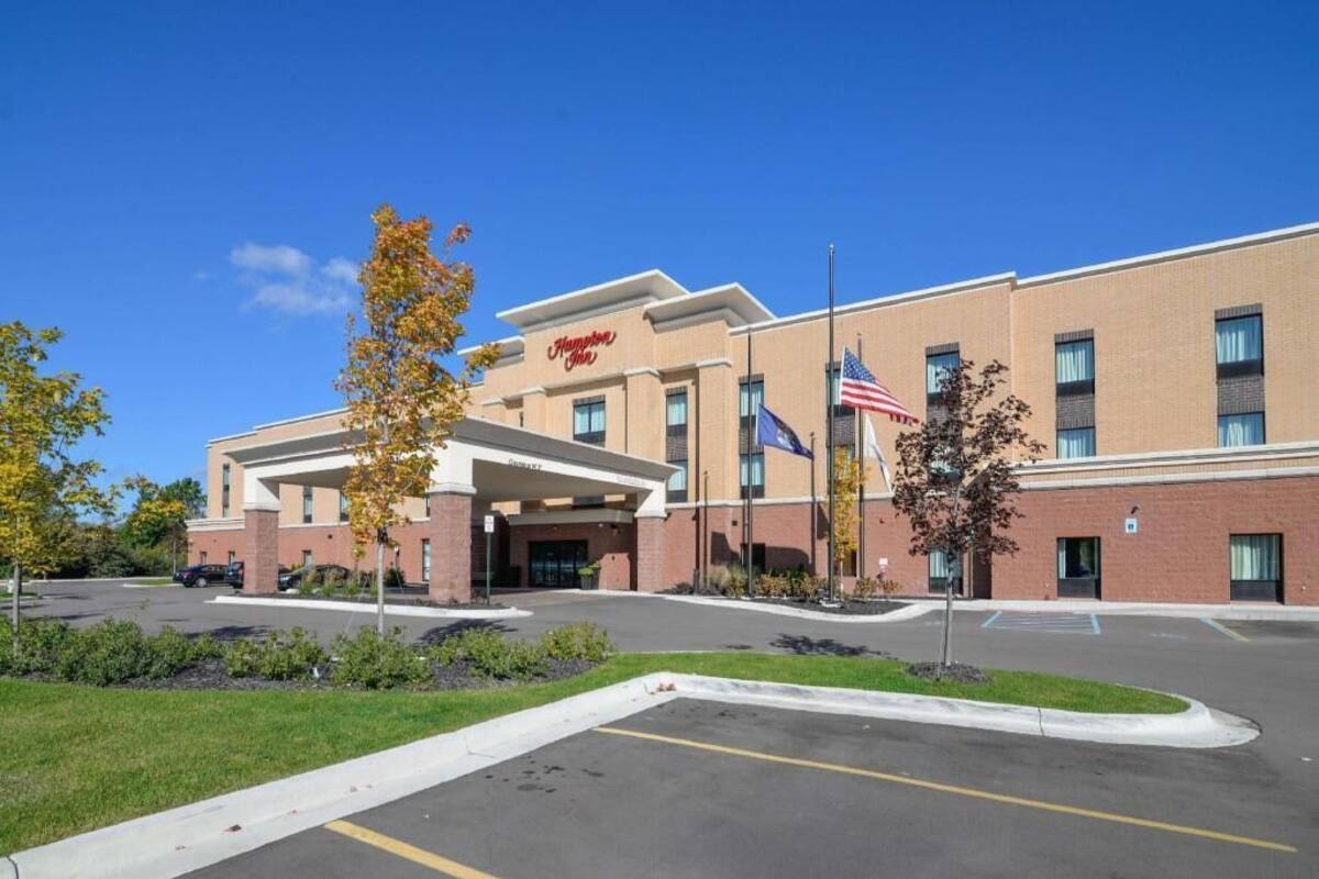 A Hampton Inn hotel with a brick facade, American flags, and a parking lot.