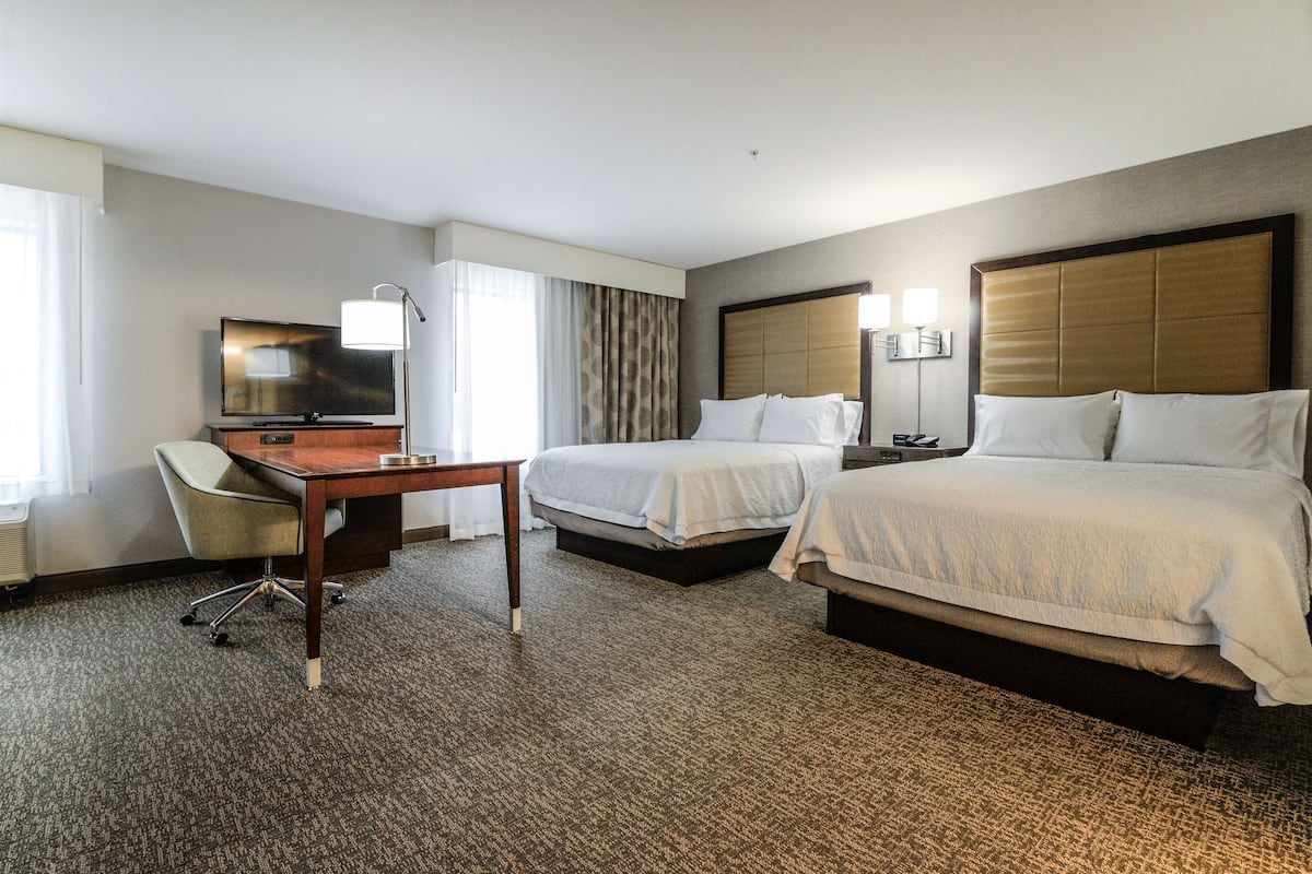 A hotel room with two beds, a desk, a television, and a lamp.